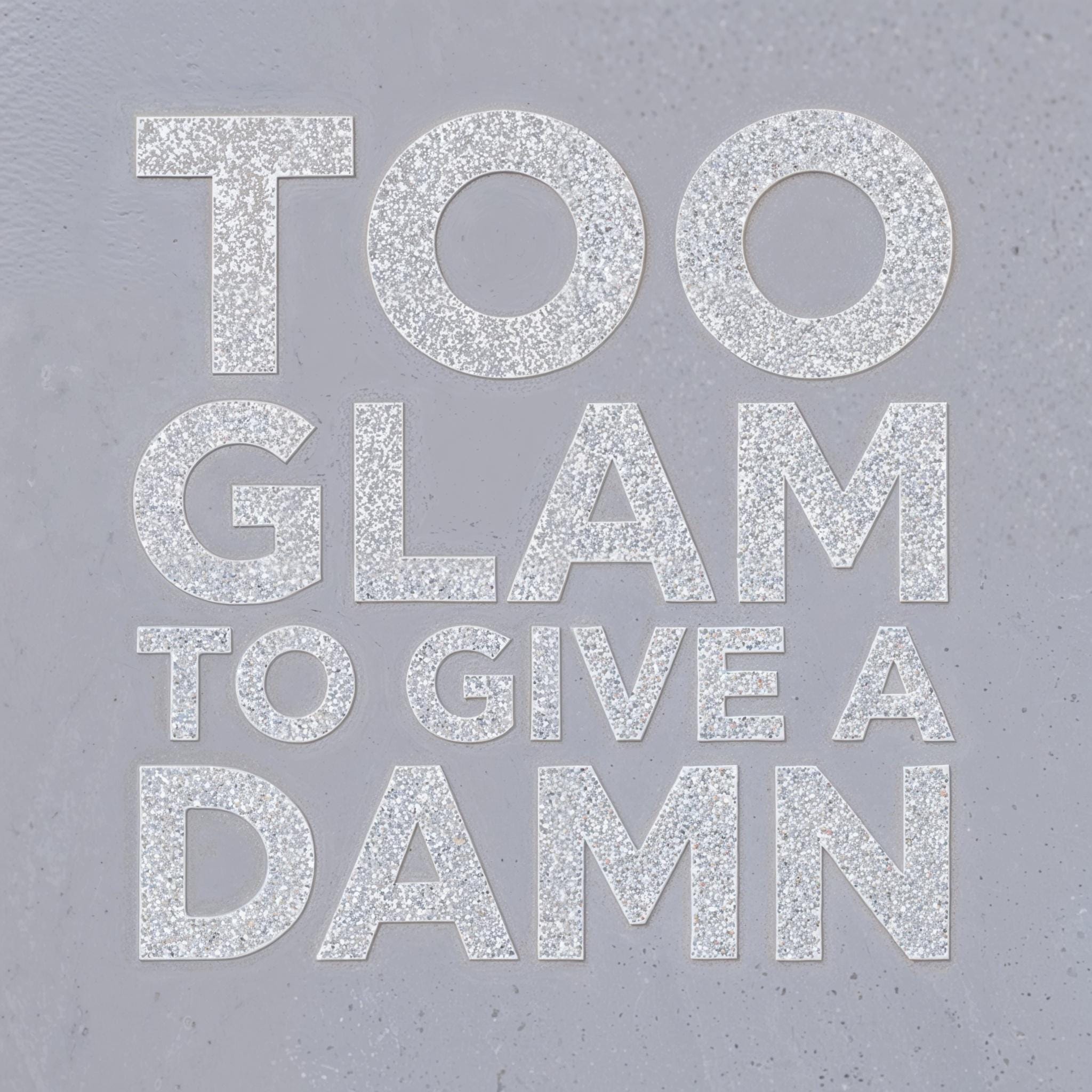 Silver glitter typography spelling “TOO GLAM TO GIVE A DAMN” on a cool grey background